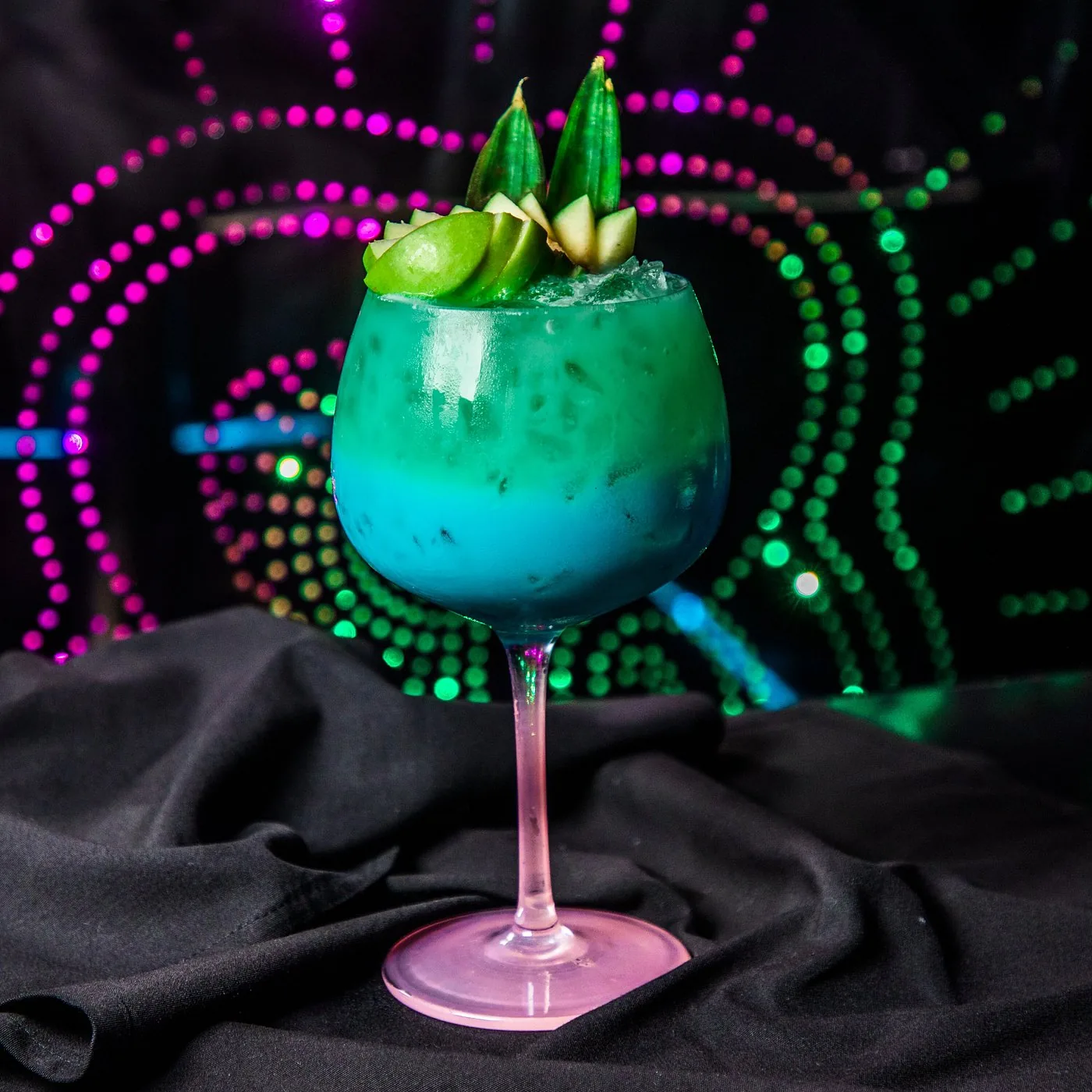 Blue signature cocktail with fresh garnish under neon lights
