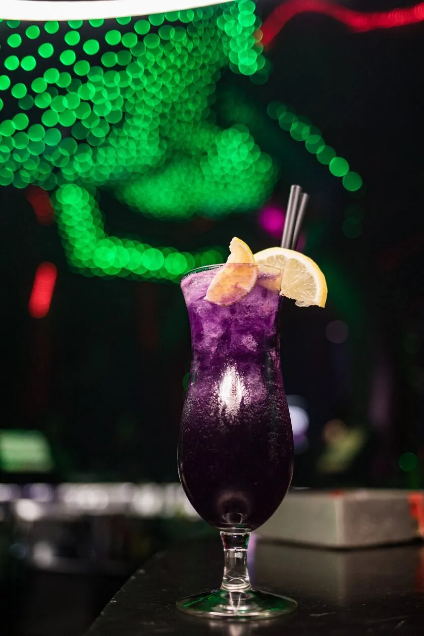 Purple cocktail with a lemon wheel against green bokeh lights