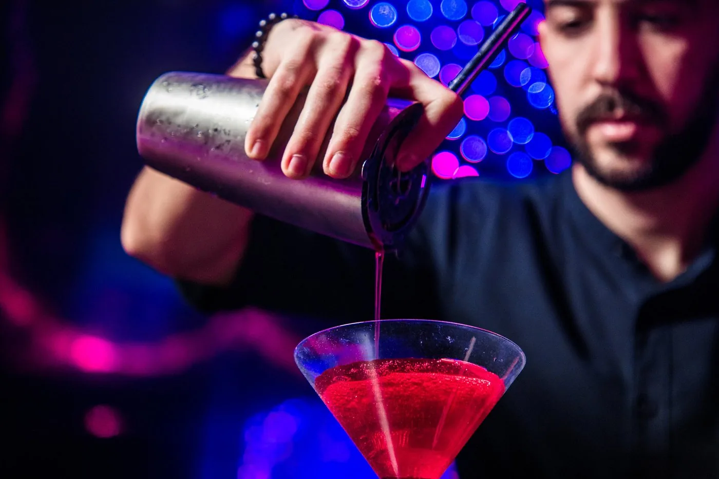Bartender pouring a red cocktail from a shaker